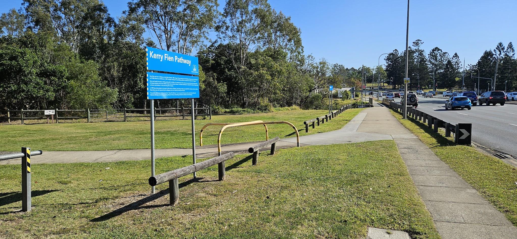 This shows the end of the Kerry Fien Pathway, where the Downfall Creek Bikeway stops at Gympie Road. Downfall Creek passes under the road next to the trees in the background.